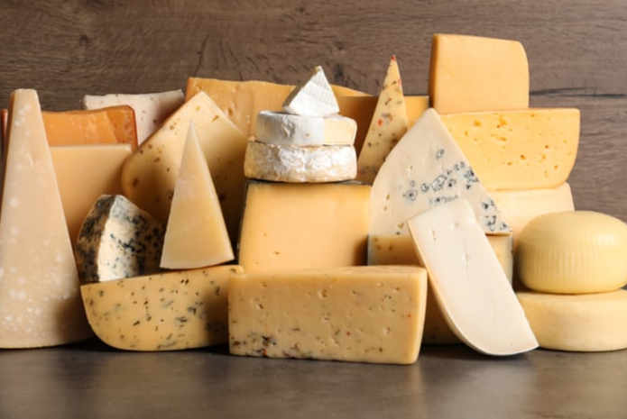 Various cheese wedges stacked on a wooden background